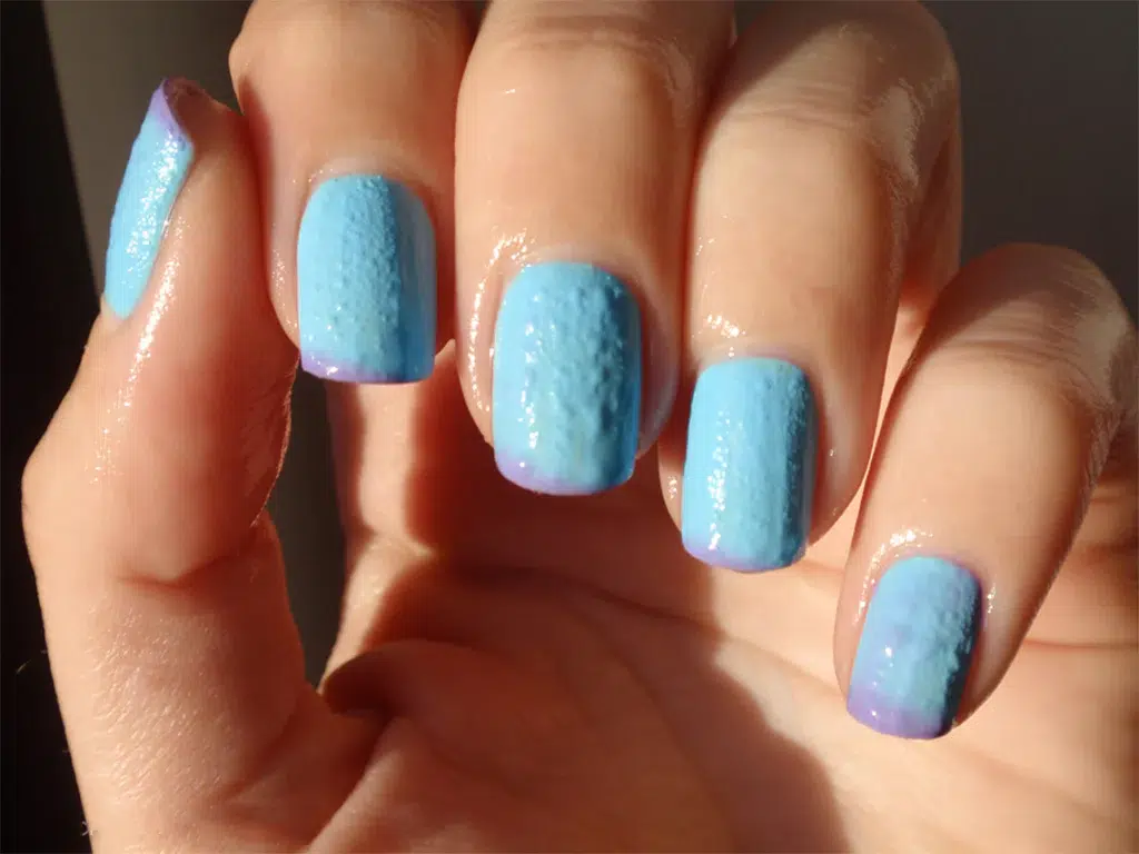 „Nepovedená manikúra – modrý lak s viditelnými bublinkami na povrchu nehtu“